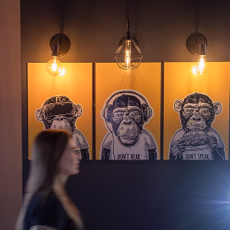 Imagem de parede com quadros e lâmpada, com uma mulher passando na frente